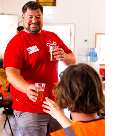 A man passes a cup of beer to another man to taste