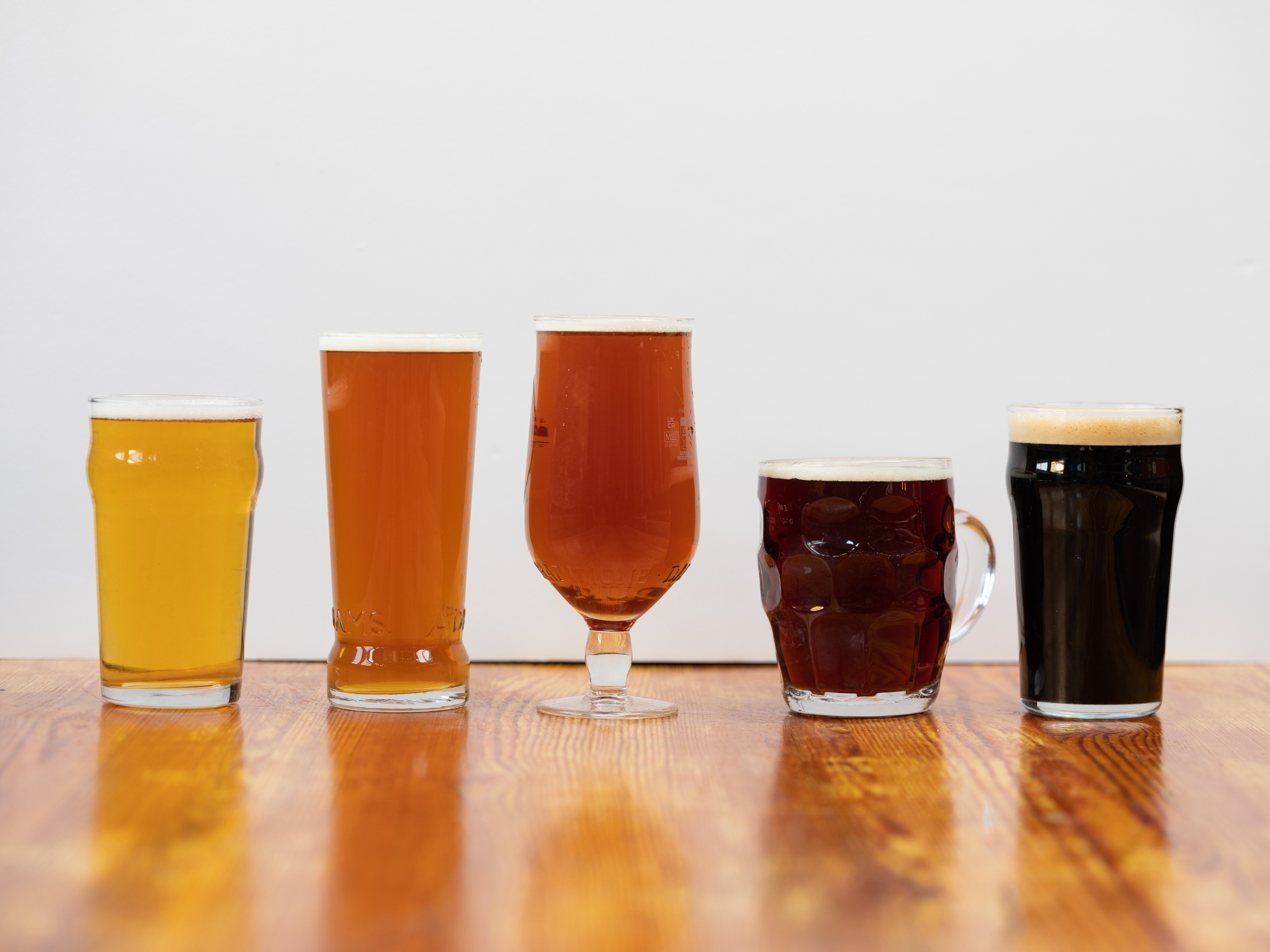 A line up of beer glasses on a table filled with beers from pale ales to bitters