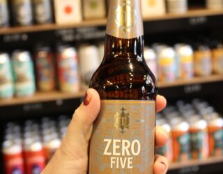 A bottle of No Alcohol beer being held in front of a shelf of beer bottles.