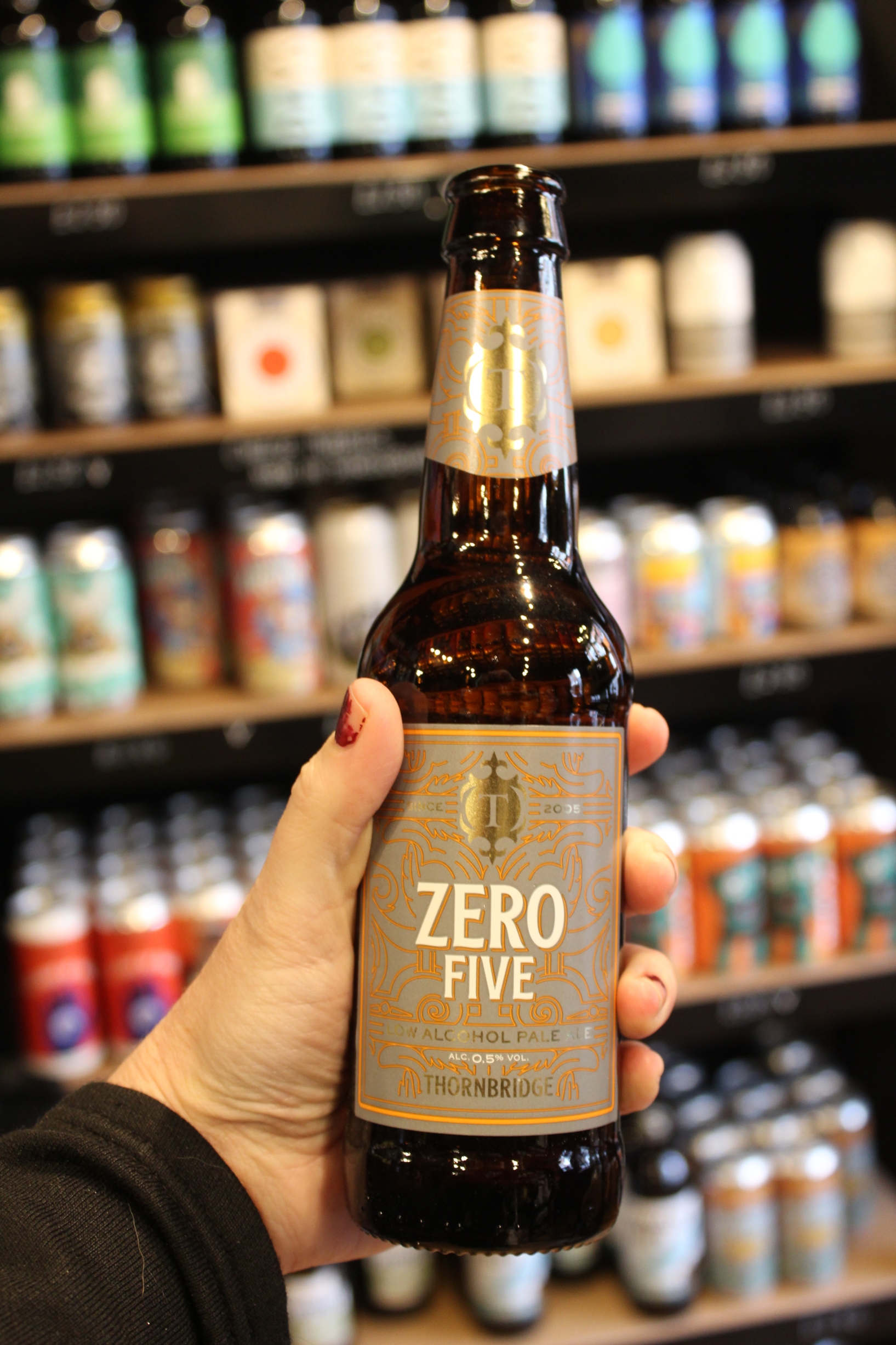 A bottle of No Alcohol beer being held in front of a shelf of beer bottles.