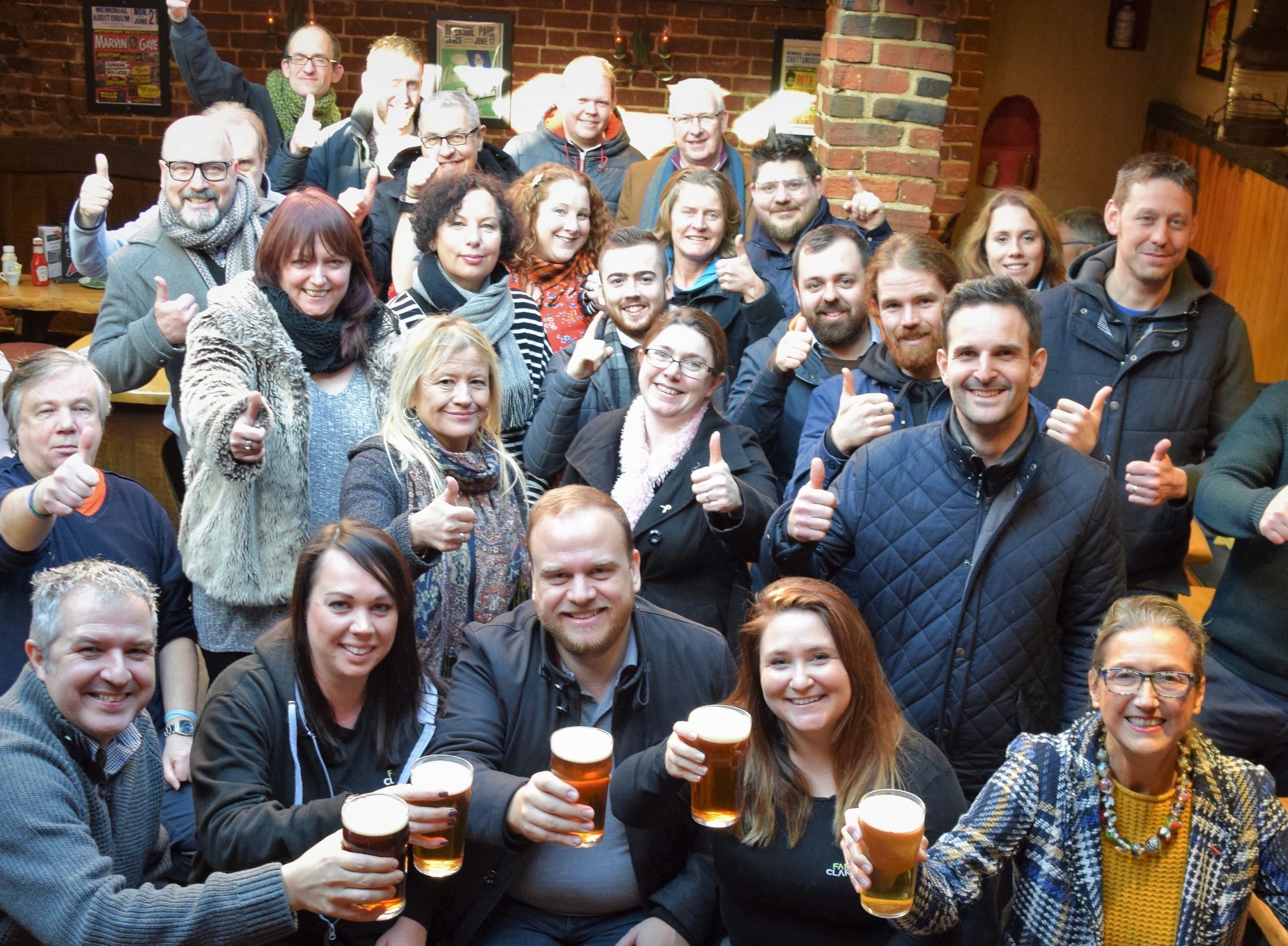 Cheers to cask ale week 2024. A group of beer drinkers raise a pint of cask ale in celebration.